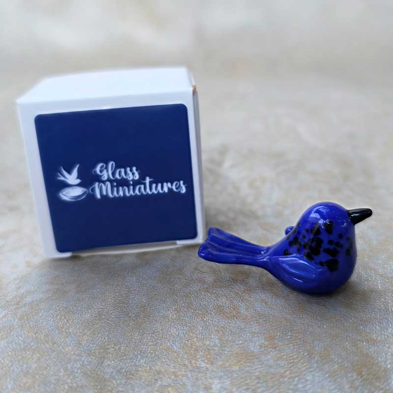 The Chic Nest handblown glass blue wren miniature figurine with black details next to a small white gift box